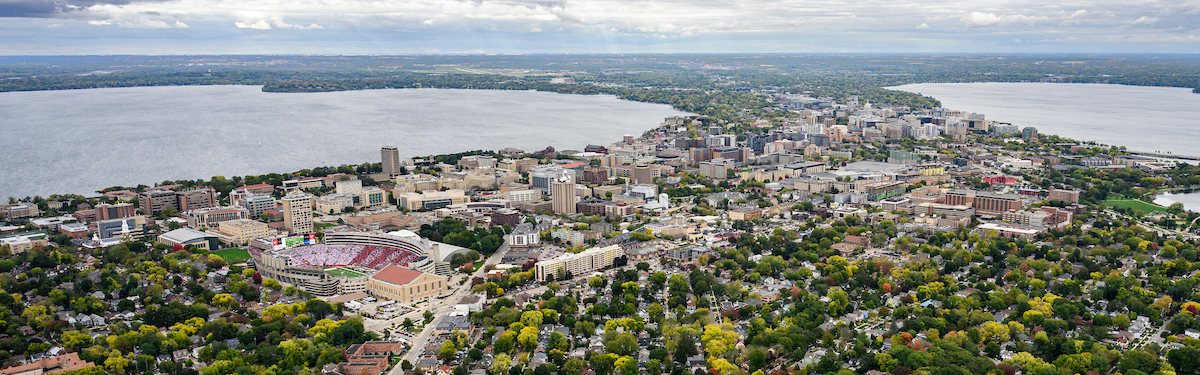 A photo of Madison, WI taken from the sky on a gray-clouded day. Green trees and lakes are visible.